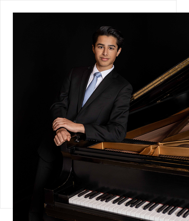 Man in a suit standing by a grand piano.
