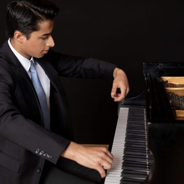 A young man in a suit playing the piano with focus.